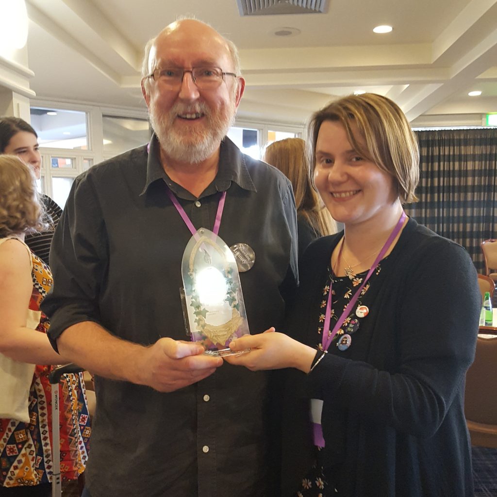 Bearded man standing next to a woman, both holding an award plaque.